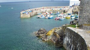 Un pueblo costero con barcos amarrados en un muelle de piedra, agua cristalina y un muro de piedra.
