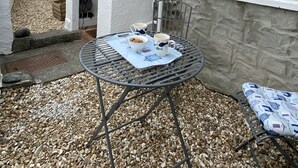 Un patio con una mesa preparada para dos personas, un muro de piedra y una ventana con detalles azules.