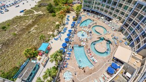 Ein Luftbild eines Hotels mit mehreren Schwimmbecken, Liegestühlen und einem Strandbereich.