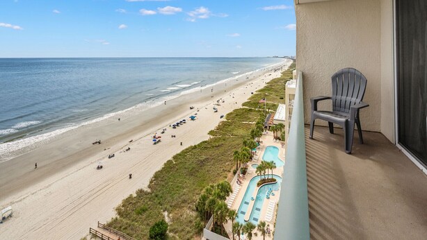 Een balkon met uitzicht op een strand, een zwembad en een stoel.