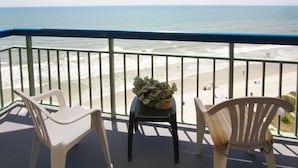 A balcony with two chairs and a table, overlooking a beach with people and waves. - Spacious oceanfront condos w/pool and sundeck-walking distance to Cherry Grove Pier (North Myrtle Beach)