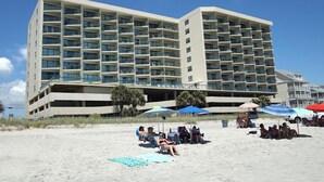 A multi-story hotel with balconies, located on a beach with people relaxing under umbrellas. - Spacious oceanfront condos w/pool and sundeck-walking distance to Cherry Grove Pier (North Myrtle Beach)