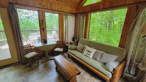 Eine Holzhütte mit einer Couch, einem Tisch, Stühlen und Blick auf einen Wald.