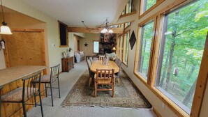 Ein gemütlicher Essbereich mit Holztisch und -stühlen, einem Teppich und Blick auf den Wald durch große Fenster.