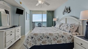 Une chambre avec un lit, une commode, une télévision, un ventilateur de plafond et une vue sur l’océan.