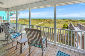 A wooden deck with two rocking chairs, a covered porch, and a view of the ocean.