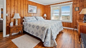 Una camera da letto con parete rivestita in legno, un letto grande con biancheria a motivi, due lampade ai comodini, un quadro appeso e una finestra con persiane.