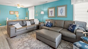 Ein Wohnzimmer mit einem grauen Ecksofa, einem gemusterten Teppich und einem Deckenventilator.