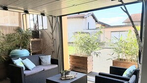 An outdoor patio with wicker furniture, a blue barbecue grill, and potted plants. - Architect House Near Lyon Eurexpo Stade Lumières (Saint-Priest)