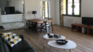 A modern living room with a dining area, a kitchen in the background, and a large window with curtains. - Architect House Near Lyon Eurexpo Stade Lumières (Saint-Priest)
