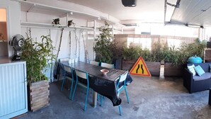 A covered outdoor dining area with a table and chairs, surrounded by potted plants and a seating area with cushions. - Architect House Near Lyon Eurexpo Stade Lumières (Saint-Priest)