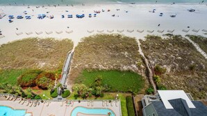 Luchtbeeld van een strandresort met een zwembad, strandparasols en een boardwalk naar het strand.