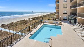 Une piscine avec vue sur la plage et l’océan, un poste de surveillance pour les sauveteurs et un bâtiment doté de balcons.