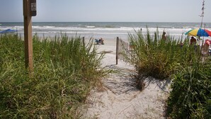 A sandy beach path leading to the ocean, with a wooden signpost and a beach umbrella in the background. - Great oceanfront view, big balcony, & condo resort with pool & hot tub in popular Cherry Grove Beach (North Myrtle Beach)