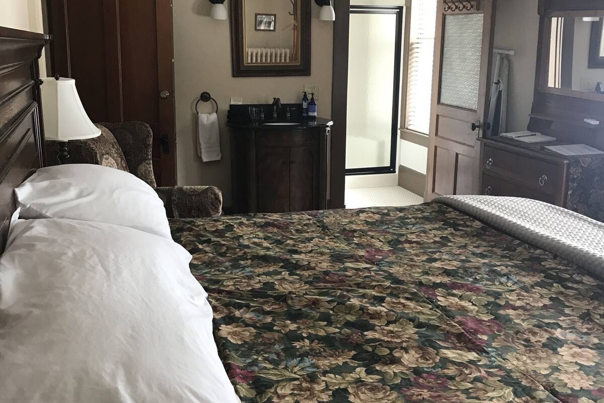 A bedroom with a large bed, a dresser, a mirror, and a door leading to another room.