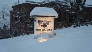 Letrero cubierto de nieve para el Bed & Breakfast Maplecroft, con un edificio de ladrillo al fondo.