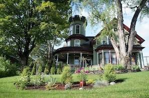 A large, historic house with a turret and wrap-around porch, surrounded by a well-maintained garden.