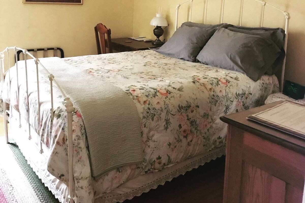 A bedroom with a bed, a chair, a desk, and a lamp.