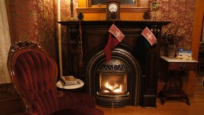 Una habitación con chimenea, un sillón rojo, una mesita redonda con libros y un reloj en la repisa.