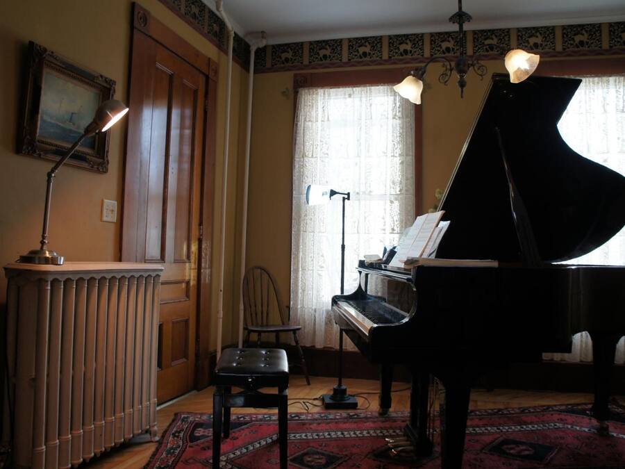 A room with a grand piano, a radiator, a chair, and a rug.