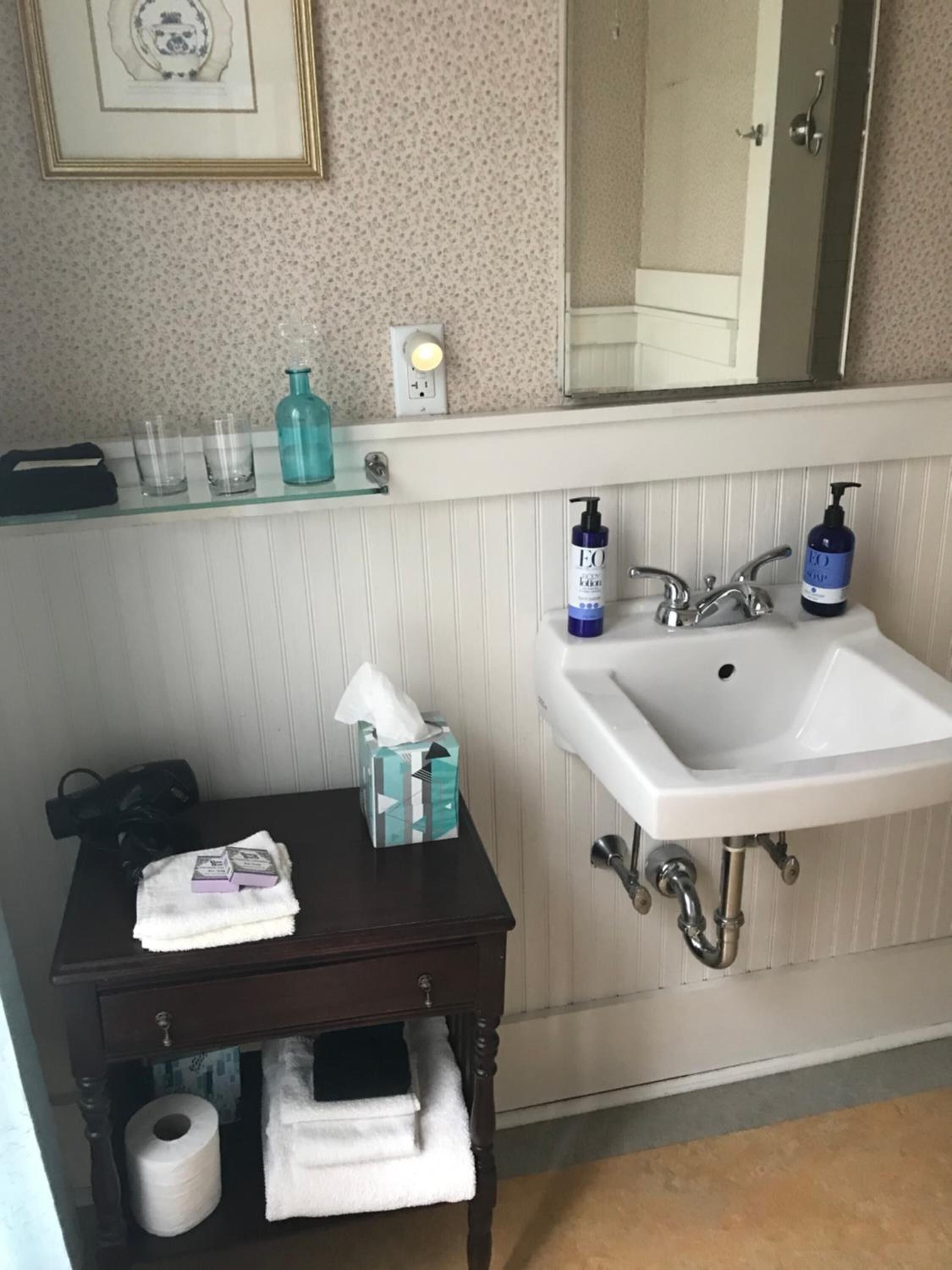Ein Badezimmer mit einem weißen Waschbecken, einem Spiegel darüber und einem kleinen Tisch mit Toilettenartikeln.