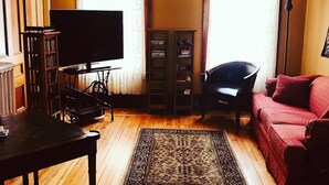 Una sala de estar con televisión, piano, un sofá rojo y una estantería.