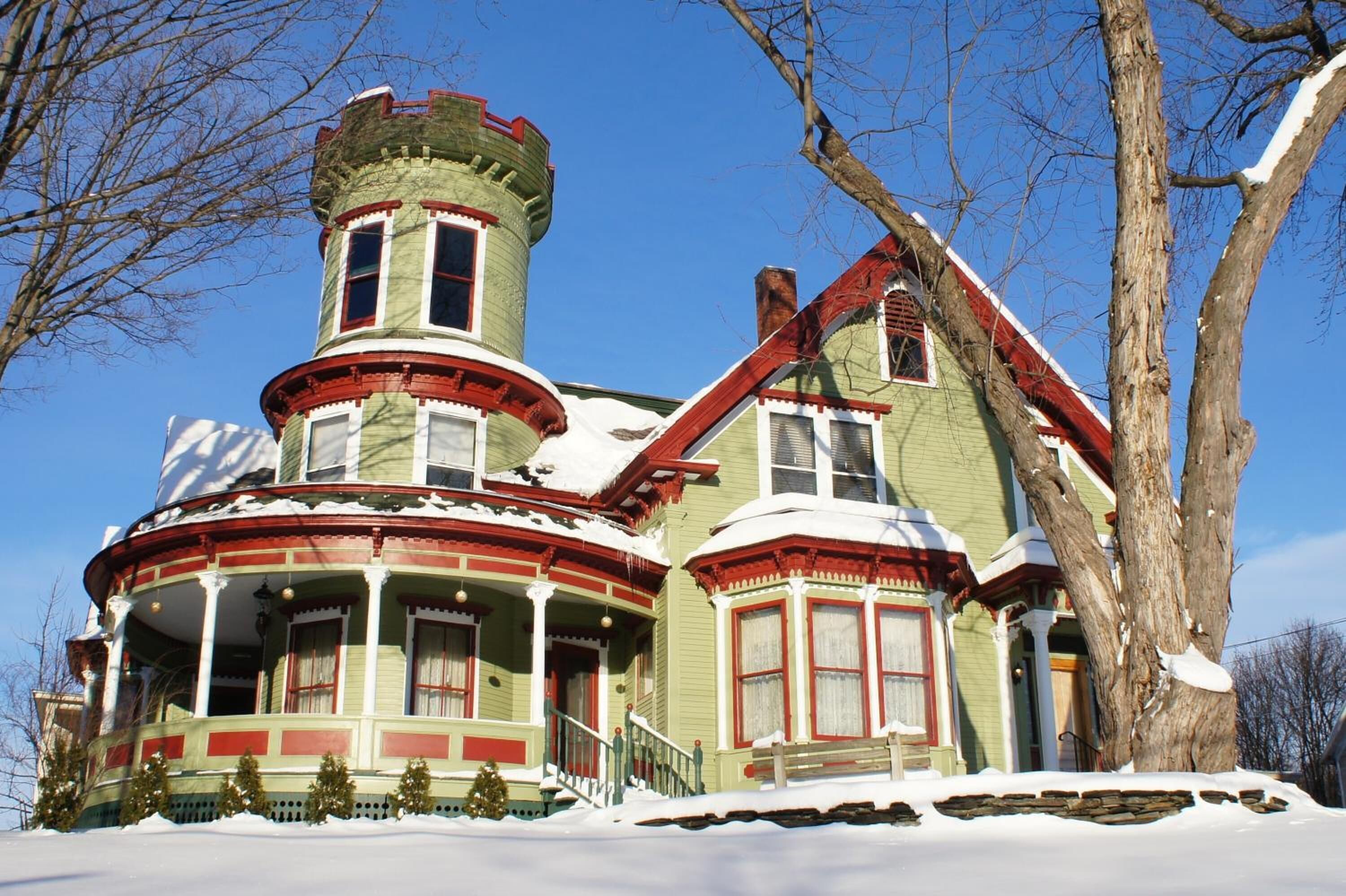Una casa de estilo victoriano con torreta, ventanas amplias y techo cubierto de nieve.