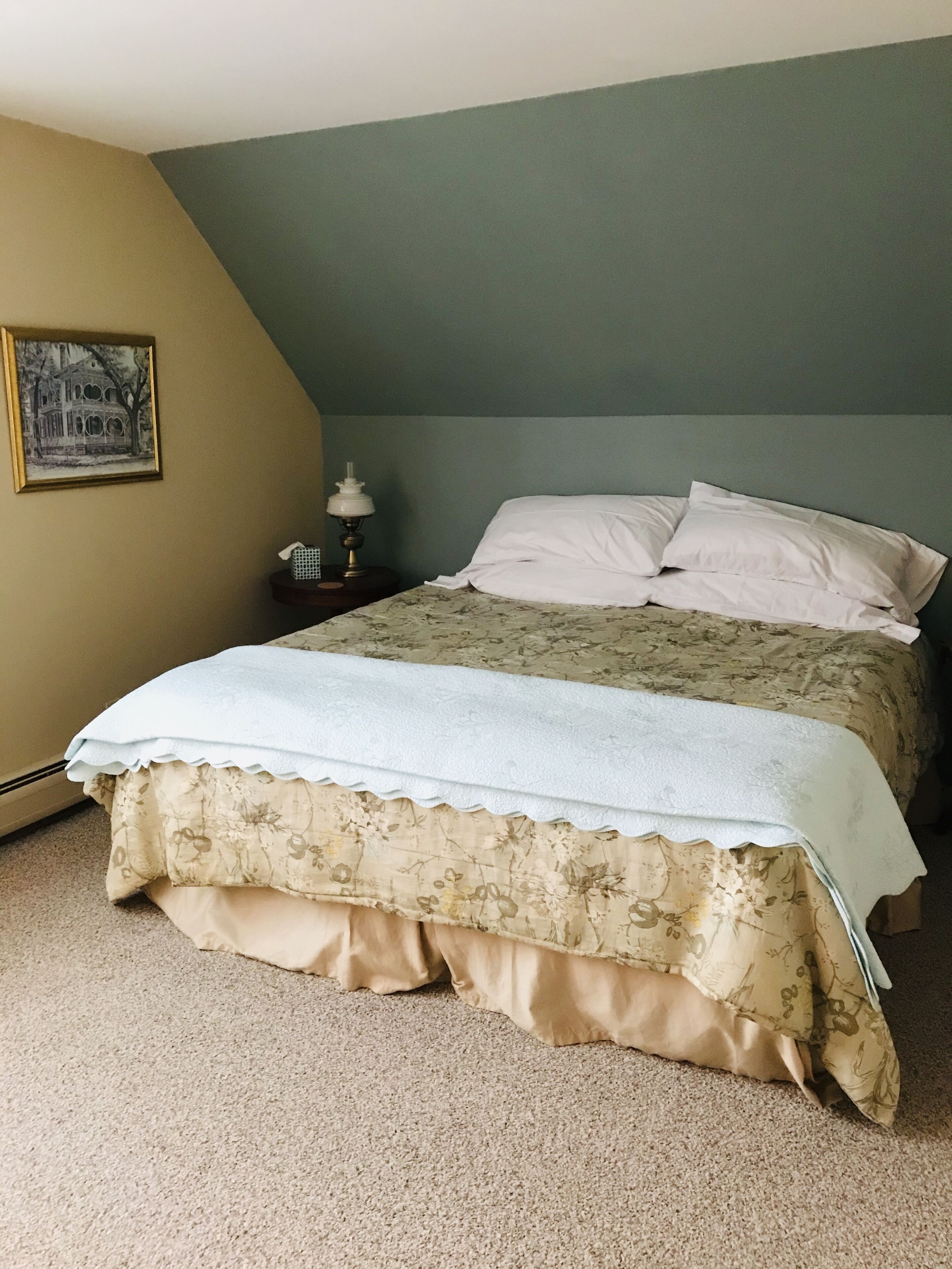 A bedroom with a bed, a nightstand, a lamp, and a framed picture on the wall.