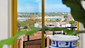 Vista desde una ventana sobre un pueblo costero con edificios, vegetación y una playa.