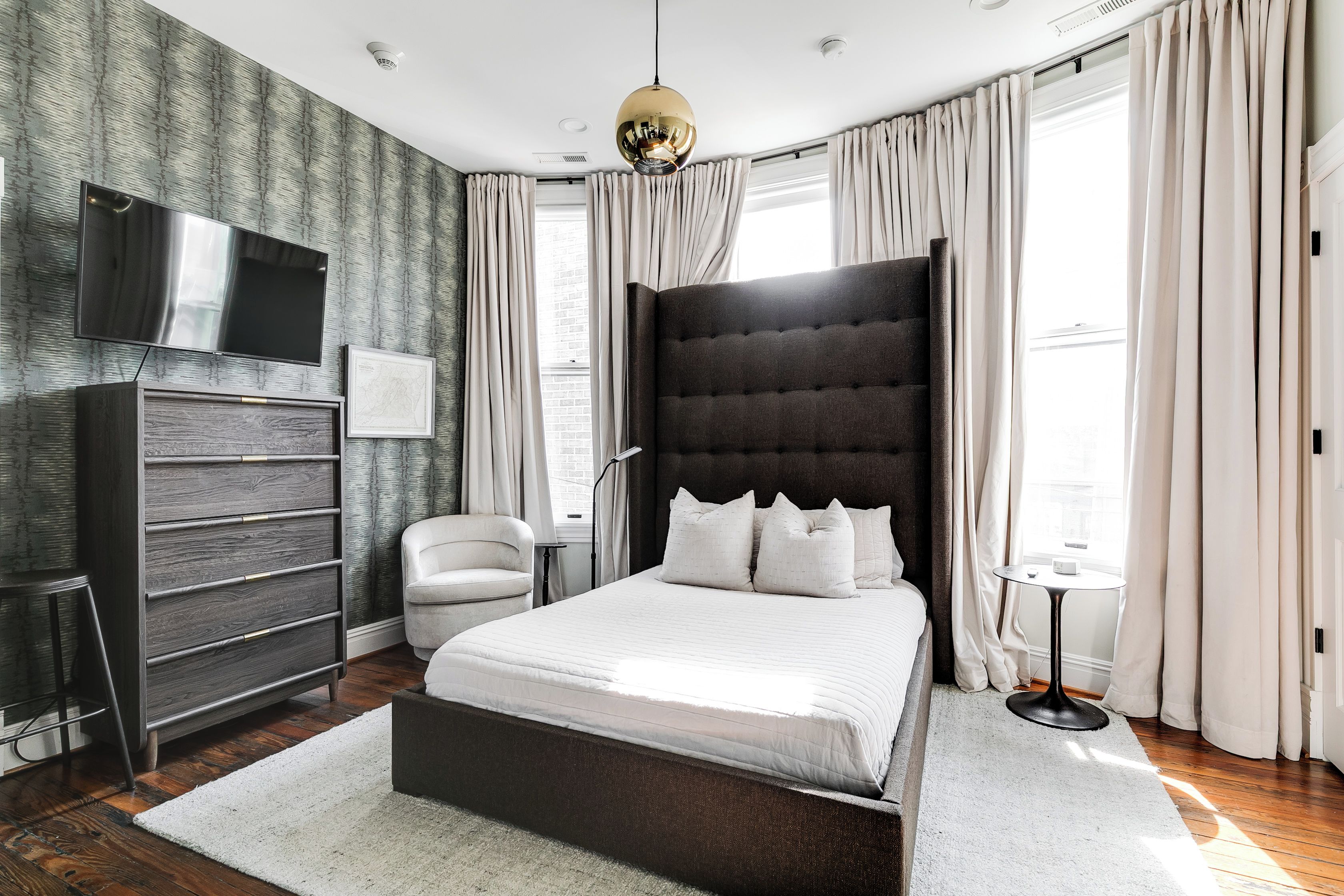 A modern bedroom with a large bed, a flat-screen TV, a desk, and a chair.