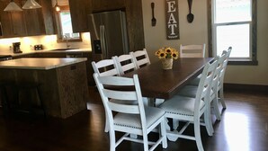 Una cocina moderna con armarios de madera, un refrigerador de acero inoxidable y un comedor con sillas blancas y una mesa.