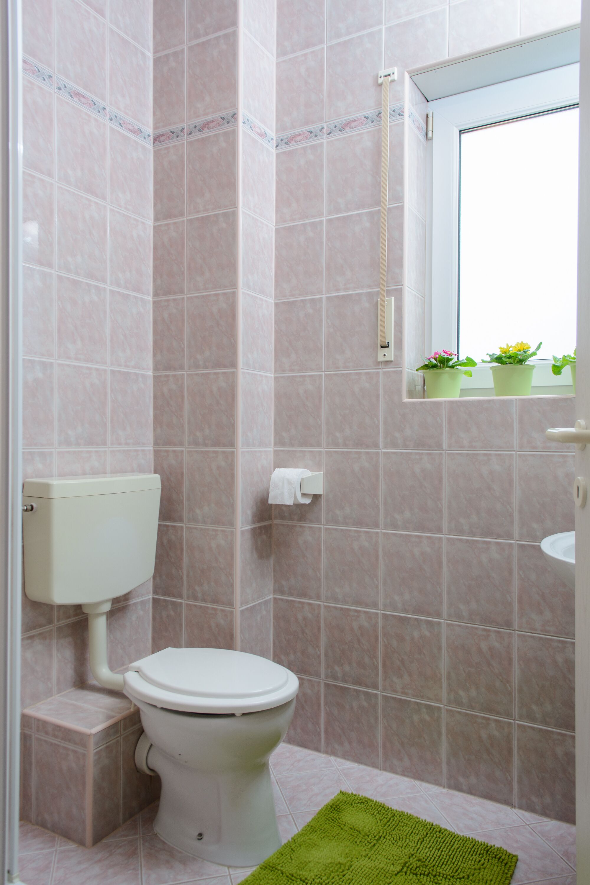 A bathroom with a toilet, a sink, and a window with a view of flowers.