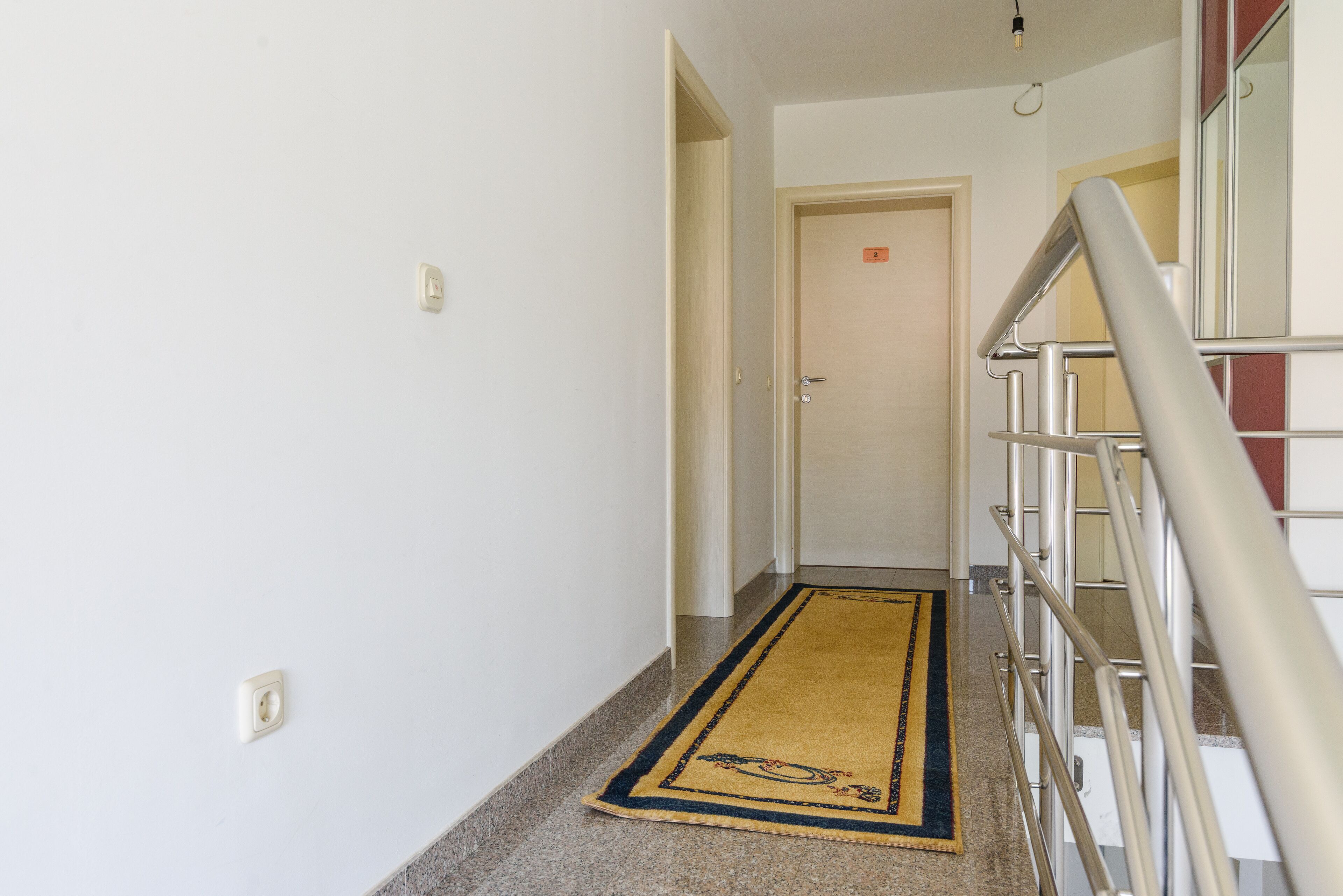 A hallway with a carpet, a door, and a staircase.