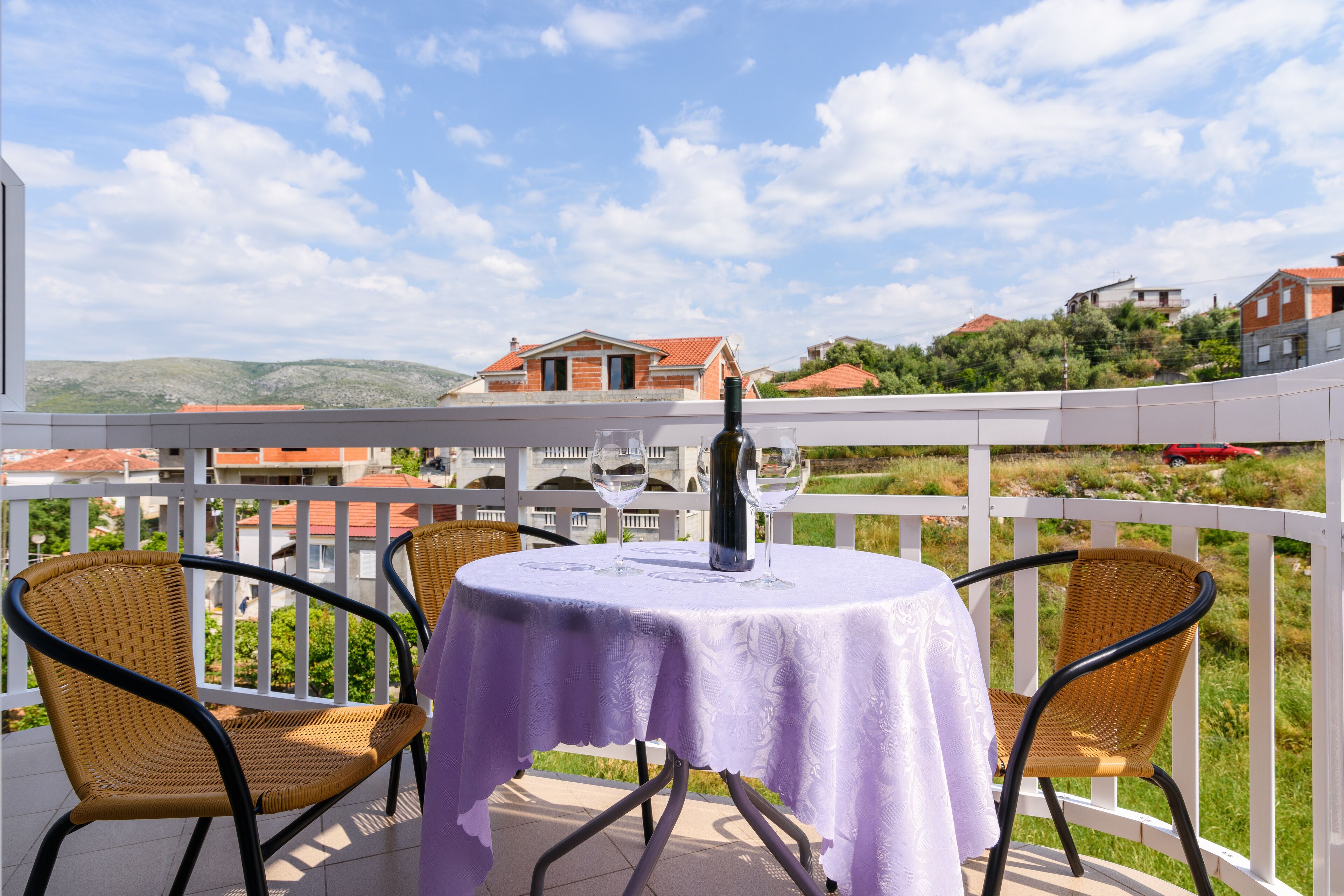 Un balcón con una mesa lista para dos personas, con vistas panorámicas a casas y colinas.