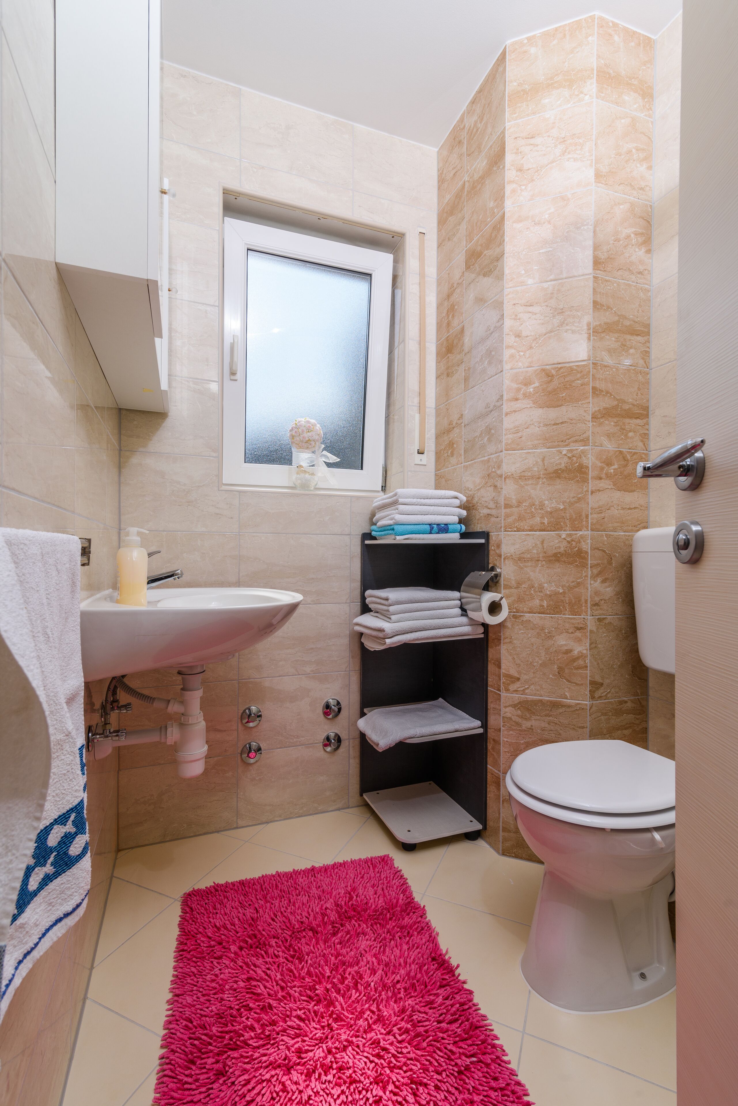 Ein kleines Badezimmer mit Waschbecken, Toilette und einem kleinen Fenster über dem Spiegel.