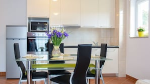A modern kitchen with white cabinets, a stainless steel oven, and a glass dining table with black chairs. - Apartmani Mijo (Trogir)