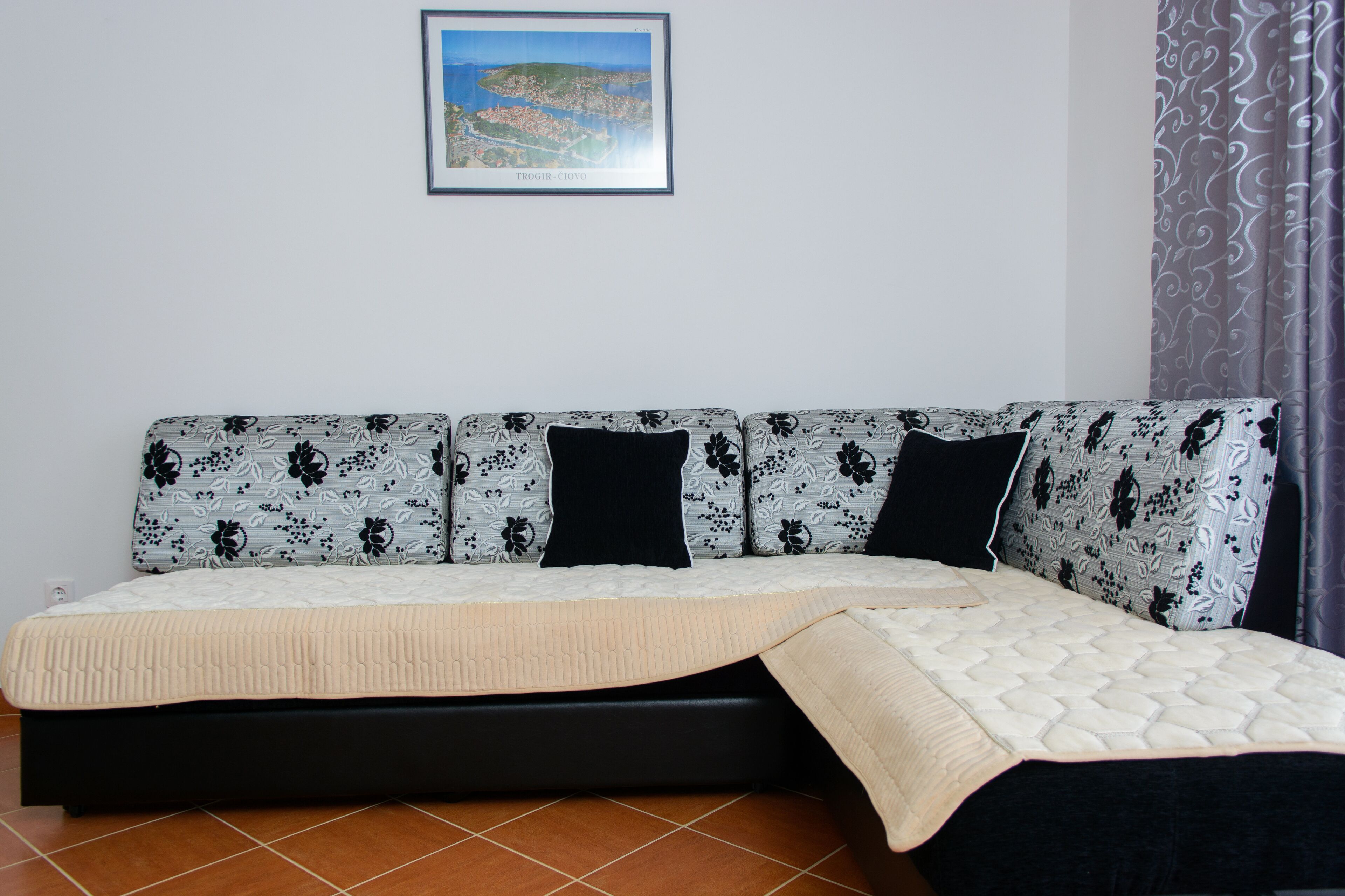 A sofa with a floral pattern, a black cushion, and a beige blanket.
