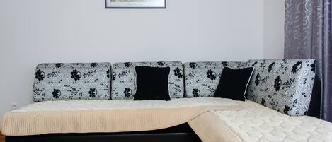 A sofa with a floral pattern, a black cushion, and a beige blanket.