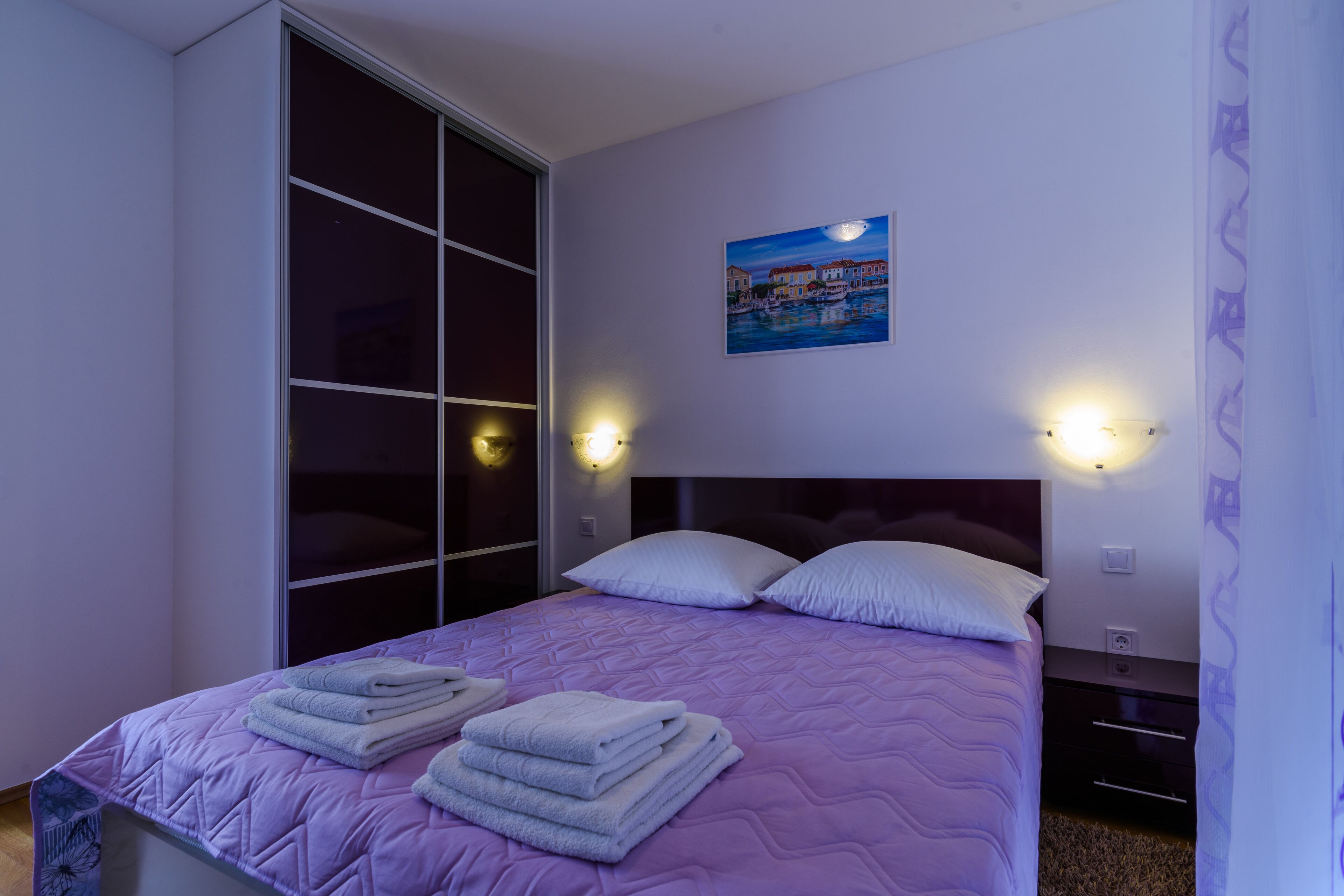 Un dormitorio con una cama, un ventanal grande y un cuadro en la pared.