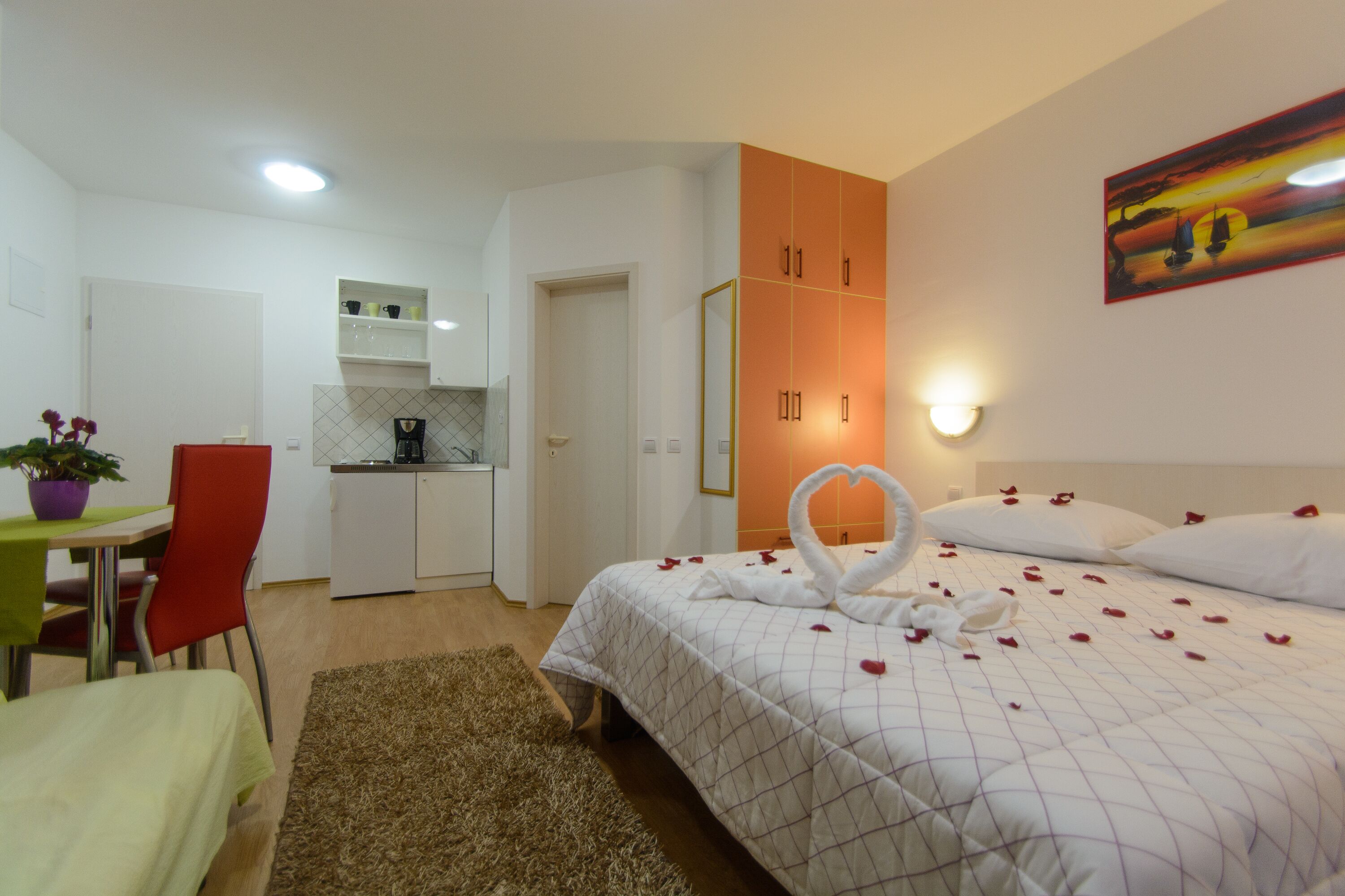 Una camera d'albergo con un letto, una scrivania, una sedia, un angolo cottura e un quadro appeso al muro.