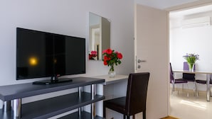 A modern room with a flat-screen TV, a mirror, a vase with red flowers, and a dining area with purple chairs. - Apartmani Mijo (Trogir)