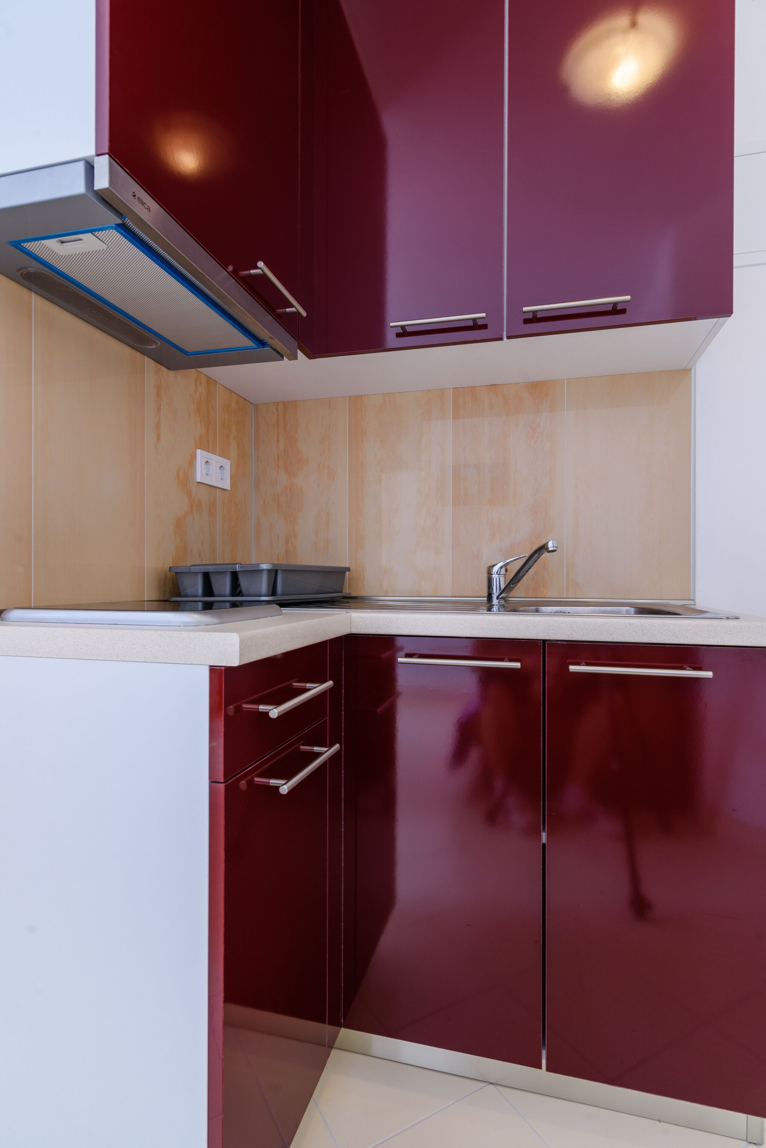 A modern kitchen with dark red cabinets, a stainless steel sink, and a built-in range hood.