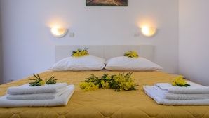A neatly made bed with white pillows and towels, a yellow quilted bedspread, and a painting of a coastal scene above the bed. - Apartmani Mijo (Trogir)