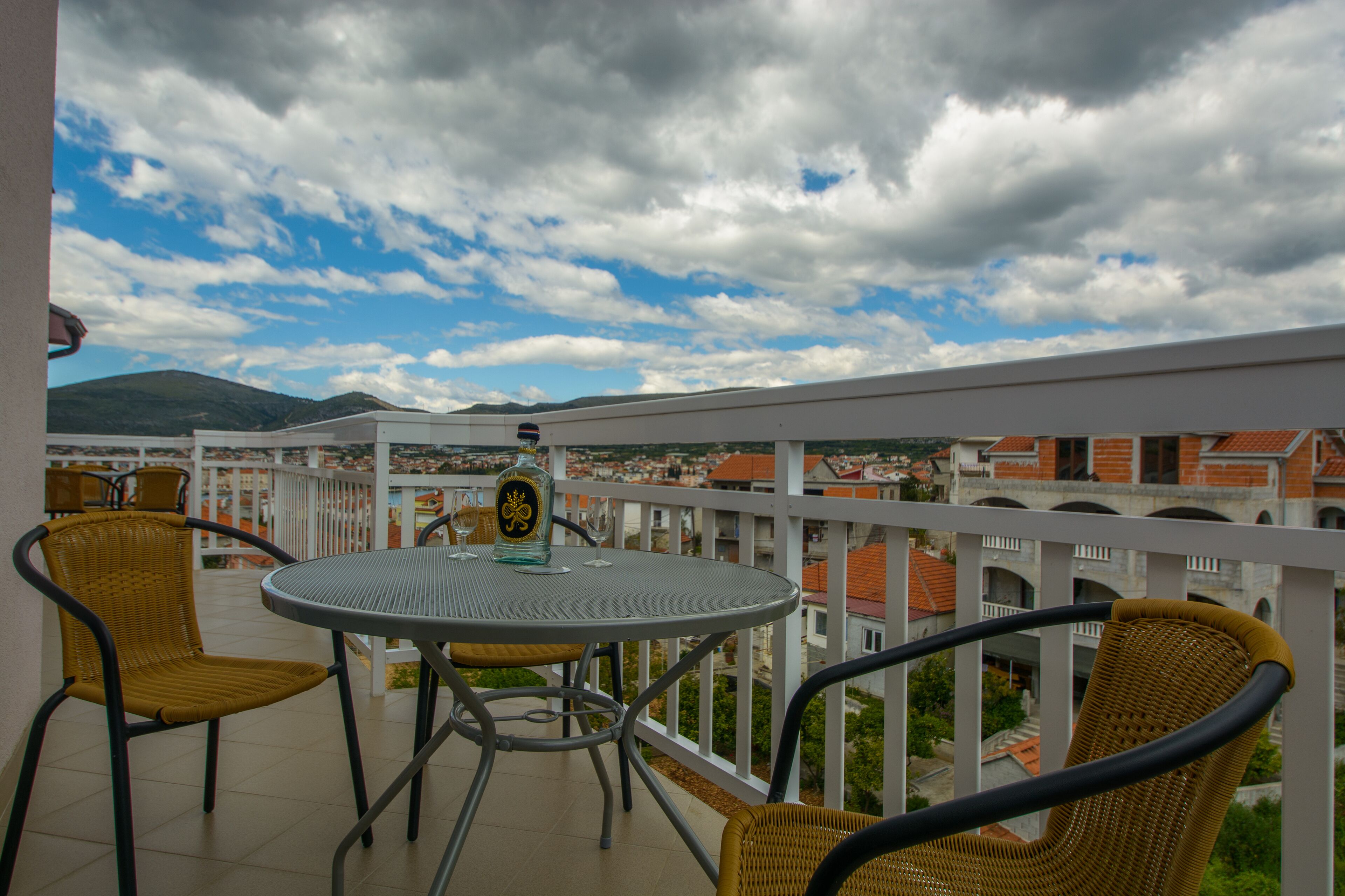 Un balcón con una mesa redonda y sillas, con vista a un paisaje urbano de edificios y montañas.