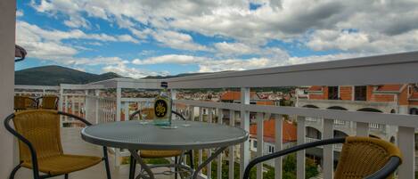 Un balcón con una mesa redonda y sillas, con vista a un paisaje urbano de edificios y montañas.