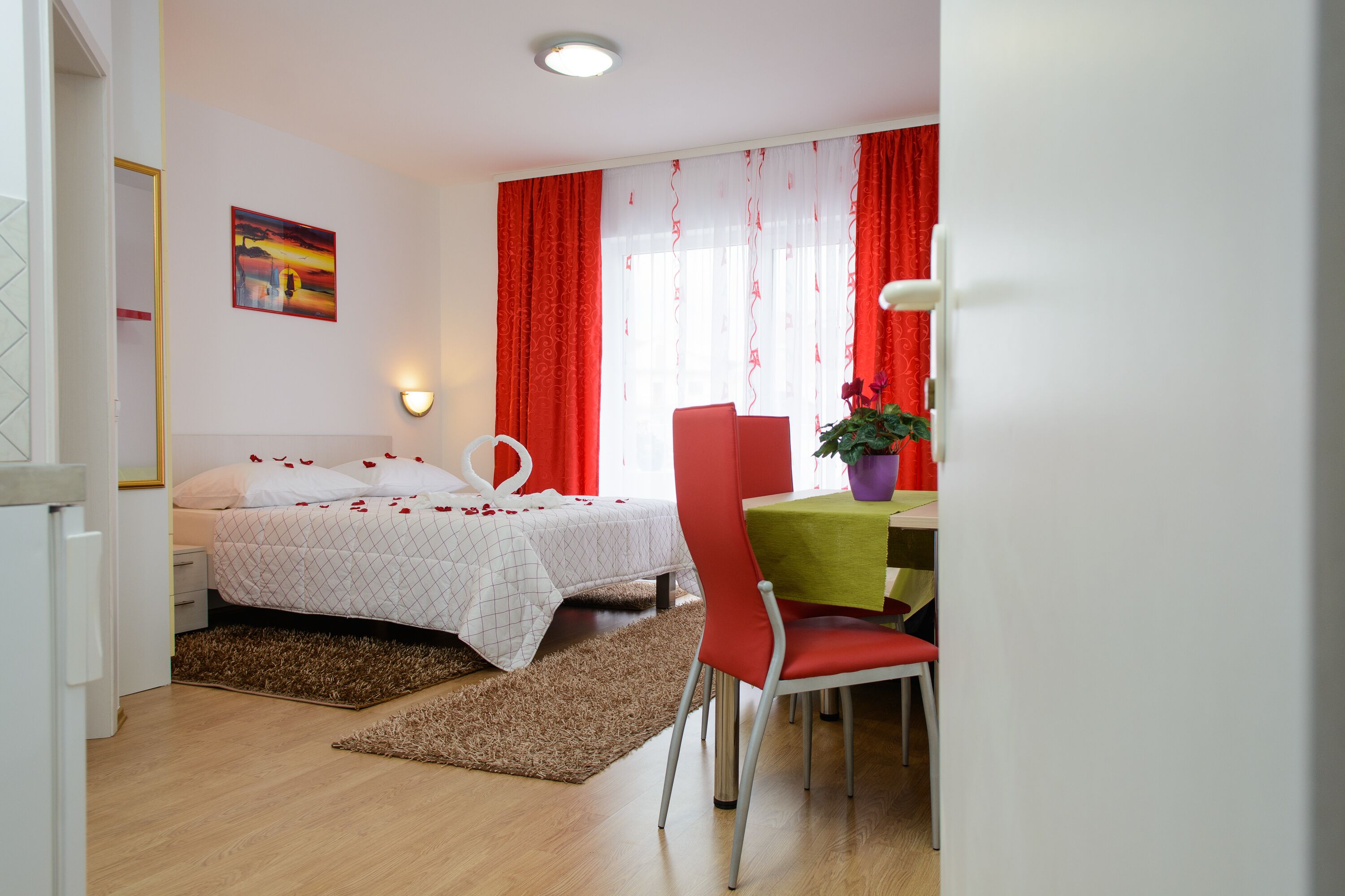Ein Hotelzimmer mit Bett, Schreibtisch mit Stuhl, Fenster mit roten Vorhängen und einer Wandlampe.