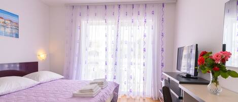 A bedroom with a bed, a desk, a chair, a TV, and a vase with flowers.
