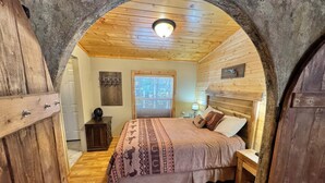 A cozy bedroom with a wooden ceiling, a bed with patterned bedding, a nightstand, and a window with blinds. -  🌲20 Min to Yellowstone, High Speed Fiber, Hot tub, Fire Pit, Play Structure. (Island Park)