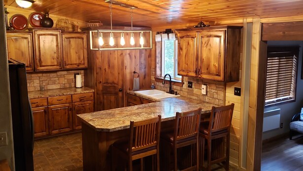 A kitchen with wooden cabinets, a granite countertop, and a central island with bar stools. -  🌲20 Min to Yellowstone, High Speed Fiber, Hot tub, Fire Pit, Play Structure. (Island Park)