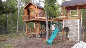 A wooden cabin with a slide and a stone building. -  🌲20 Min to Yellowstone, High Speed Fiber, Hot tub, Fire Pit, Play Structure. (Island Park)